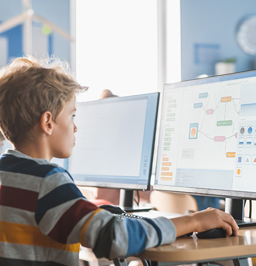 boy using computer to create diagrams in classroom environment with multiple monitors displaying educational software for learning 3d modeling concepts
